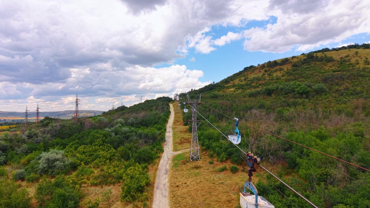 Zipline över gröna kullar på sommaren. Människor njuter av en zipline-aktivitet ovanför träd och kullar under en delvis molnig himmel en sommardag