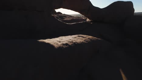 epic fpv drone shot through the needle gap in the rocky namibian desert landscape of spitzkoppe, namibia. a lone courageous woman stands between massive stones in crisp morning light.