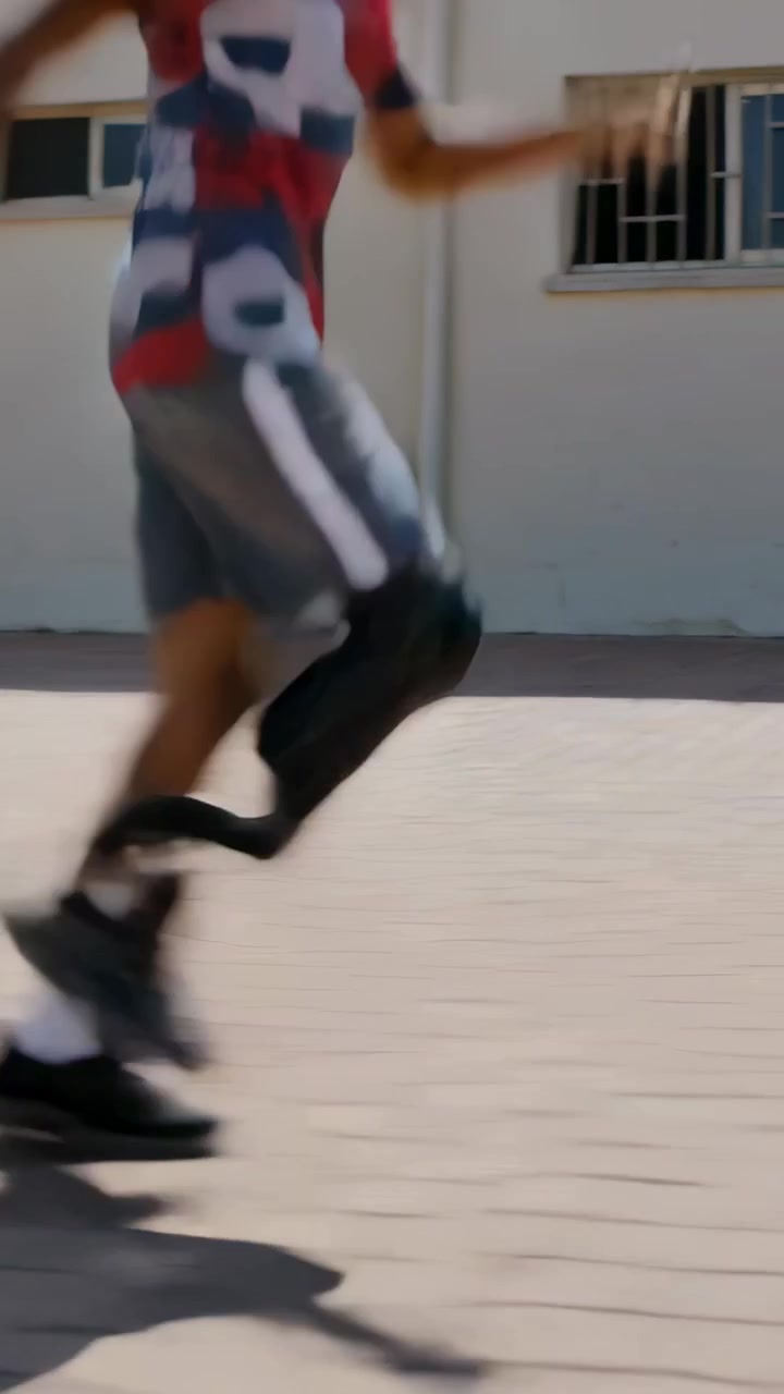 Vertical video: Sprinting man entering across courtyard in neon tee with prosthetic blade, training