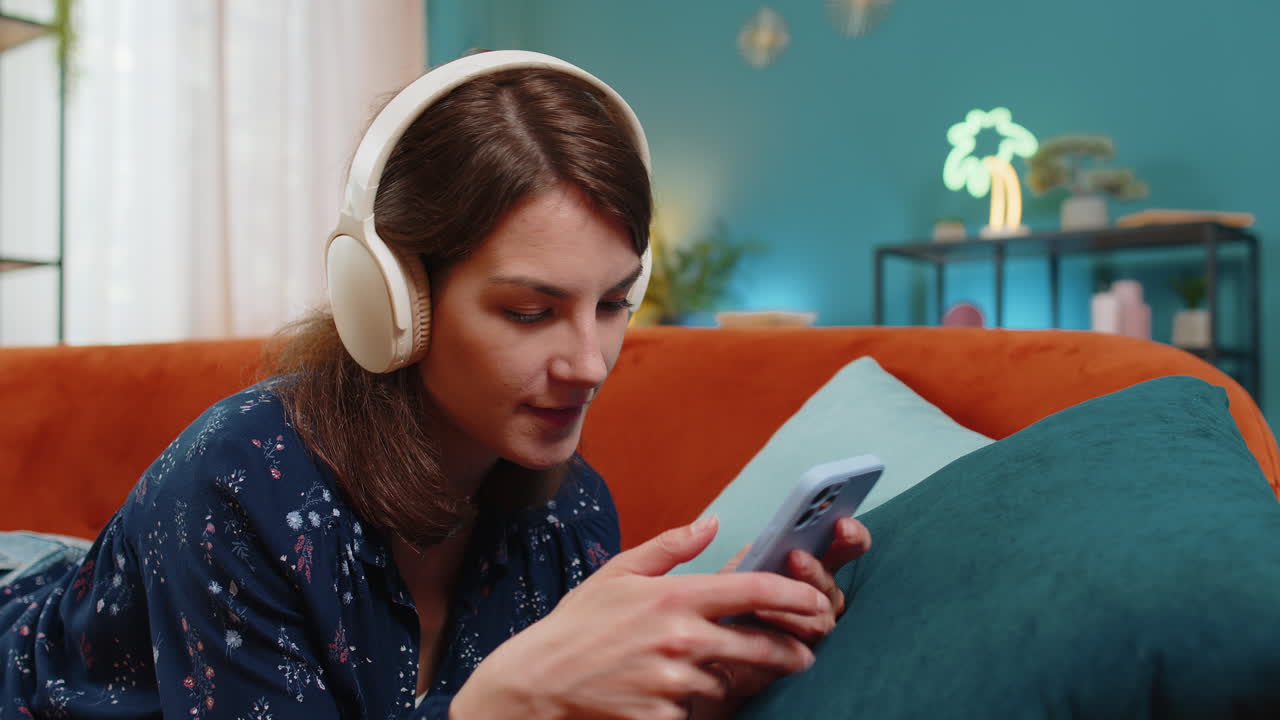 joven con auriculares inalámbricos relajándose en el sofá en casa usando un teléfono inteligente escuchando música