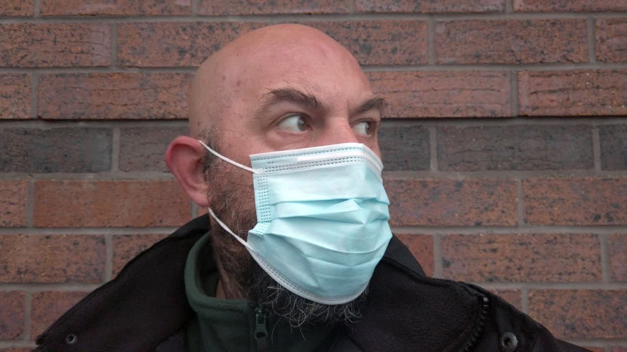 Guardia di sicurezza uomo che si sistema la mascherina medica protettiva (DPI) contro il coronavirus.