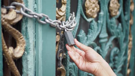 a hand reaching for a padlock on a closed gate