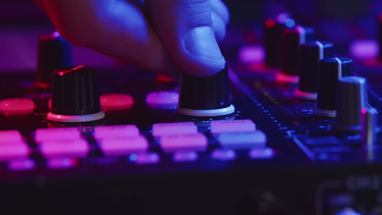 Professional DJ is adjusting fader on digital music console in pink neon light in nightclub. Male hand controls digital DJ console, closeup. Concept of party