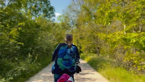 Woman-cycles-through-a-beautiful-forest-on-a-summer-day-wearing-a-blue-sweater