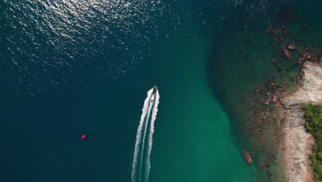 Aerial-drone-follows-motorboat-sailing-a-turquoise-green-stone-bay-in-pacific-ocean-paradisiacal-coastline