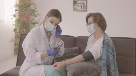 female doctor takes the pulse of an elderly patient sitting on a sofa 1