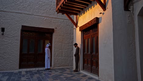 men in traditional clothing at old arabian building in courtyard at sunset.