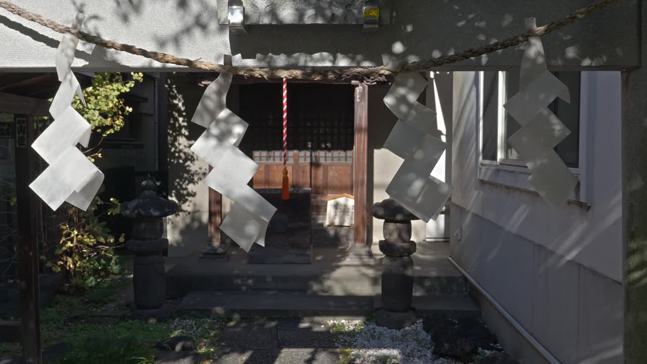 A small, traditional Shinto shrine in Tokyo, Japan, adorned with shimenawa and stone lanterns, offering a peaceful sanctuary in an urban setting.