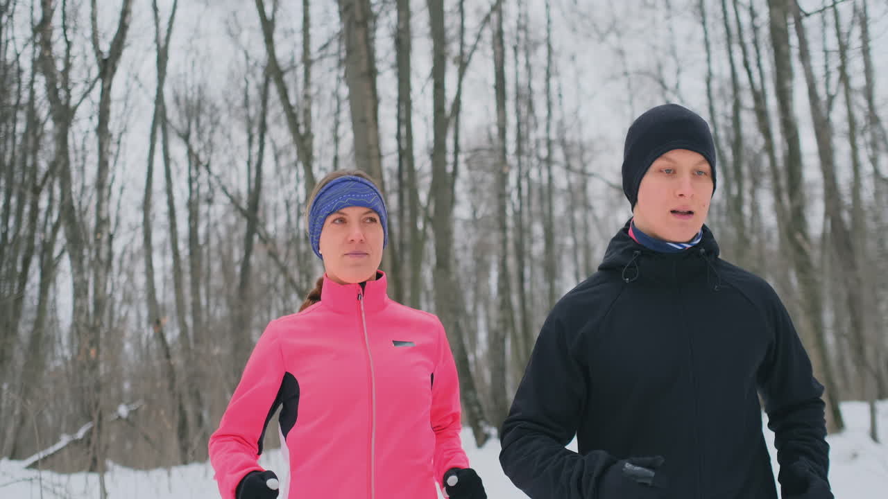 A man and a woman in a pink jacket in the winter running through the Park in slow motion. Healthy lifestyle
