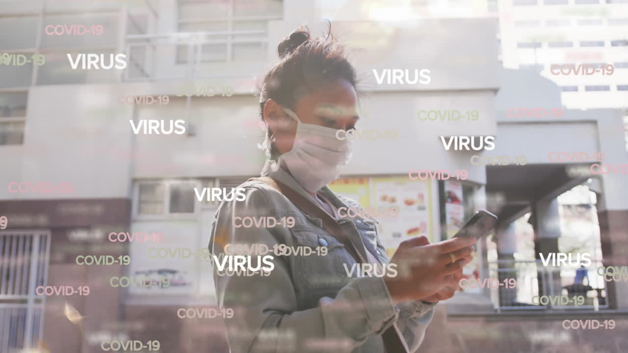 Animation of text virus and covid 19 repeated over woman in face mask using smartphone in street