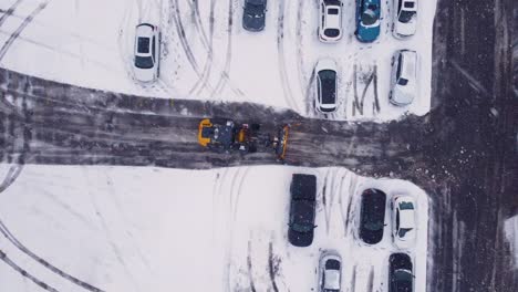 Snow-plow-tractor-cleaning-street-during-snowfall,-aerial-top-down-view