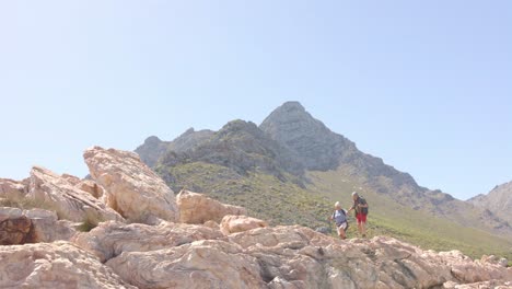 una feliz pareja biracial en las montañas haciendo senderismo con palos de trekking, en cámara lenta