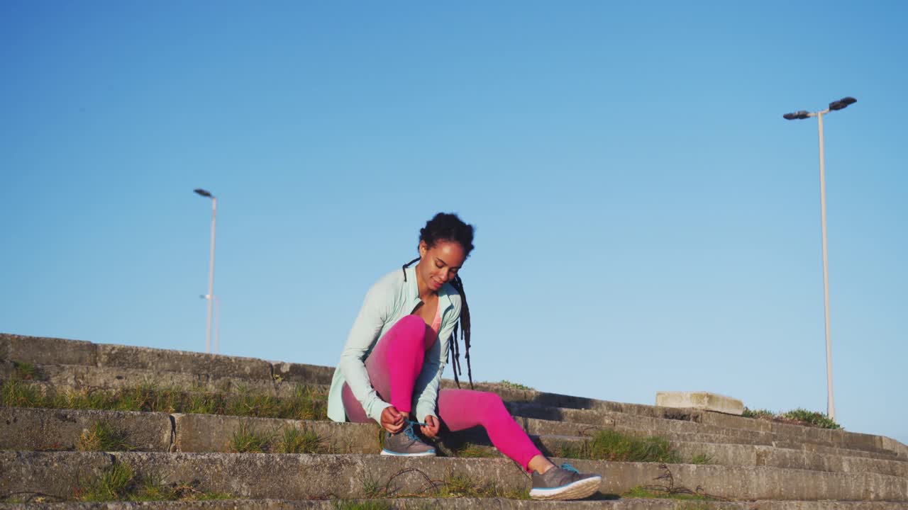 스포츠 의류 를 입은 아프리카계 미국인 여성 이 계단 에 앉아 운동 하기 전 에 준비 하고 있다