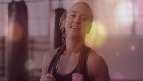 smiling woman holding jump rope with colorful light animation over gym background