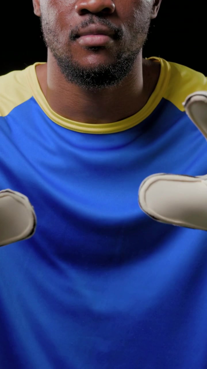 Vídeo vertical: Homem de camisa azul com as mãos empilhadas, mostrando luvas acolchoadas para melhor aderência em estúdio.