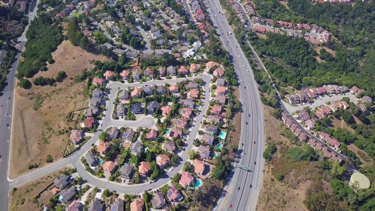 Ripresa aerea fissa di case e autostrada nei sobborghi della contea di San Mateo, area della baia di San Francisco, California, USA, la telecamera avanza