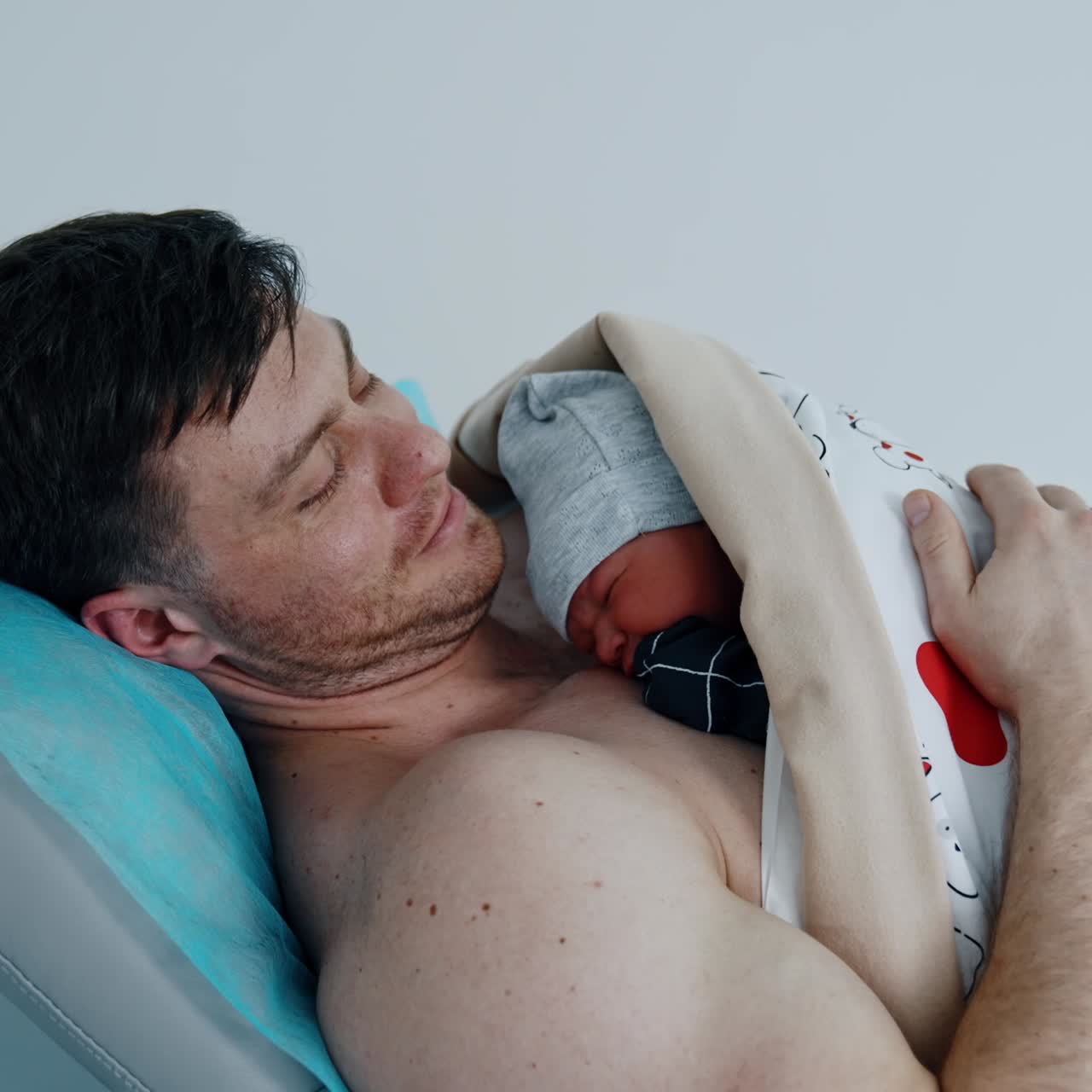 Father is happy to hold and caressing his newborn baby. The child is laid on the dad's chest right after birth