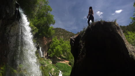 mujer joven de pie sobre una roca frente a impresionantes cascadas, vista cinematográfica de ángulo bajo