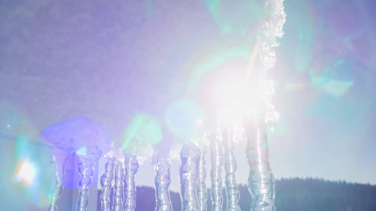 Low-angle video shot of icicles hanging from snow against a clear blue sky, capturing the contrast