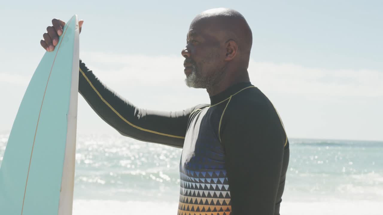 Senior african american man standing with surfboard on sunny beach
