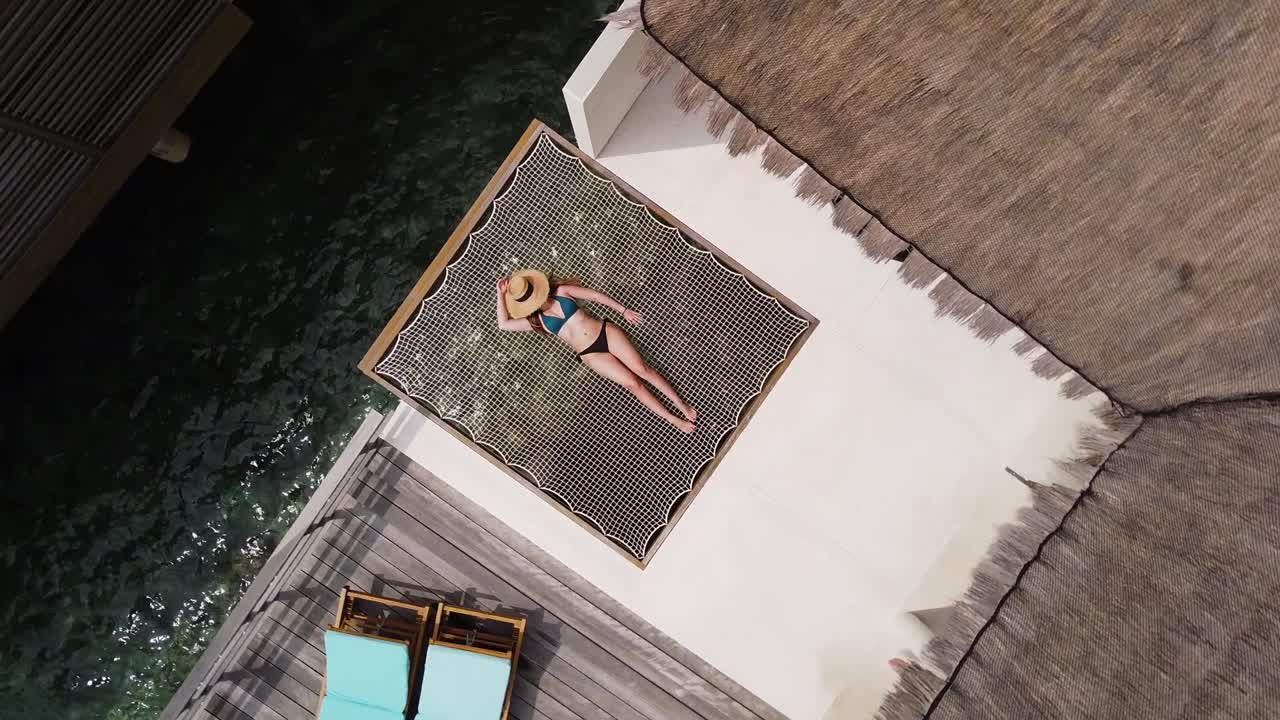 chica tomando el sol en la red en una villa de agua tropical