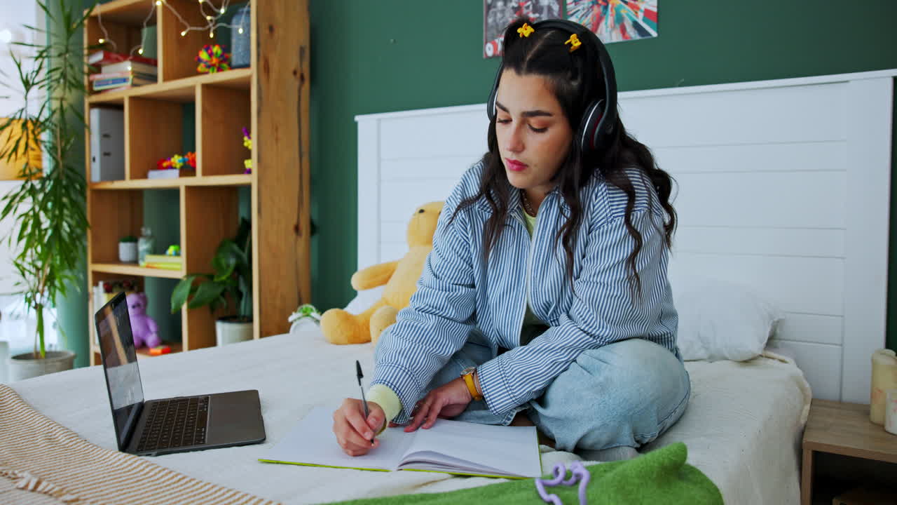 Woman studying with laptop and notebook in bedroom