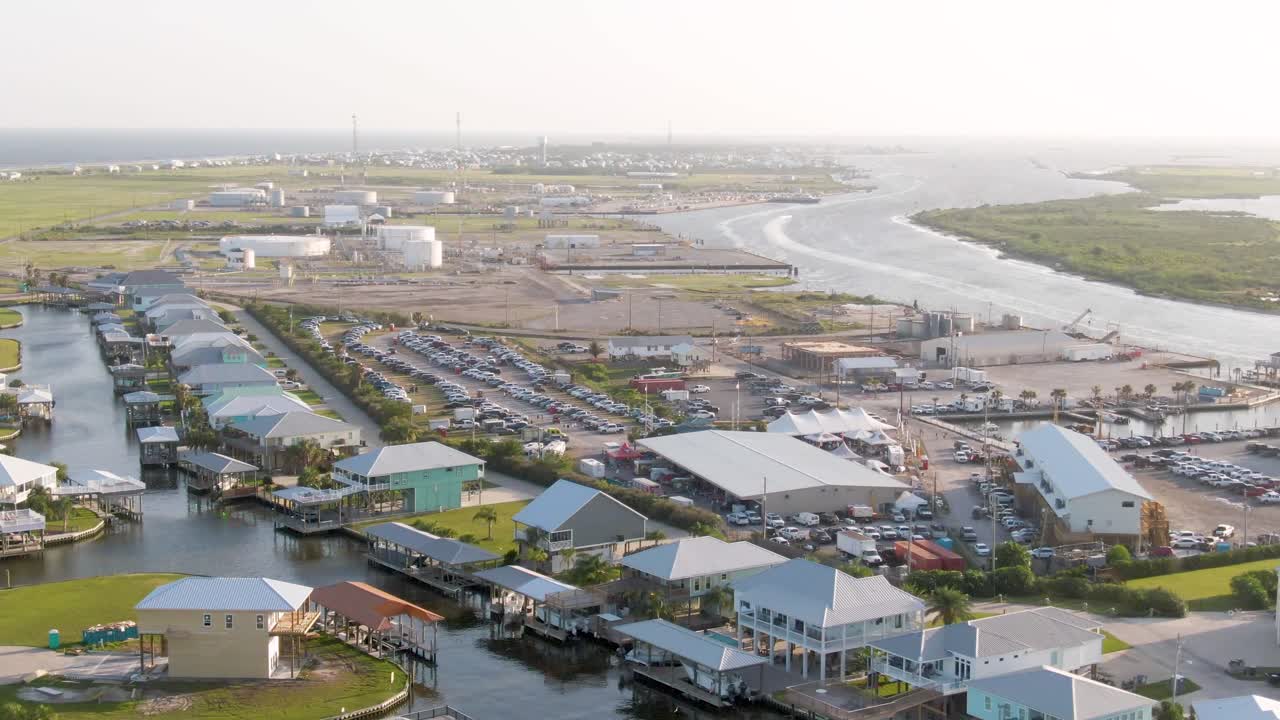 A rotating drone shot over a private gated community on Grand Isle, showing canal-front homes, boats, manicured waterfronts, and expansive views of the Island and Grand Isle Beach in the distance