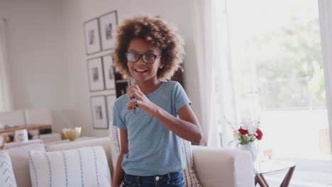 Pre-teen-African-American-girl-dancing-and-singing-at-home-using-phone-as-a-microphone,-waist-up,-close-up