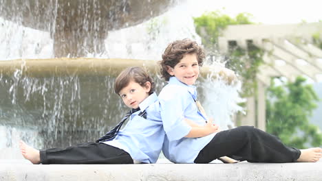 un par de niños vestidos formalmente se sientan espalda con espalda frente a una fuente