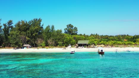 Quiet-exotic-beach-with-white-sand-bordered-by-green-tropical-trees-and-turquoise-lagoon-with-clear-calm-water-where-fishing-boats-floating-in-Jamaica