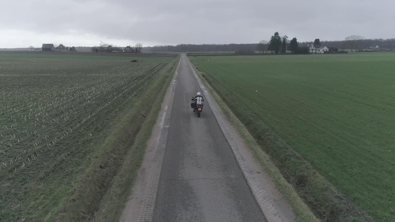 Drone following motorcyclist driving down farm fields.