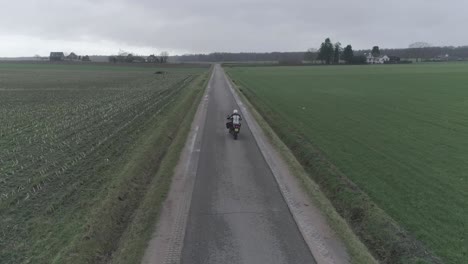 drone following motorcyclist driving down farm fields.