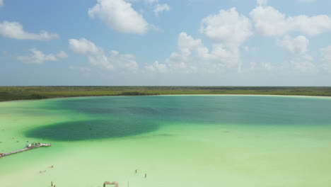 Forwards-fly-above-tropical-forest,-revealing-beautiful-natural-treasure.-People-swimming-in-pastel-green-lake.-Kaan-Luum-lagoon,-Tulum,-Yucatan,-Mexico