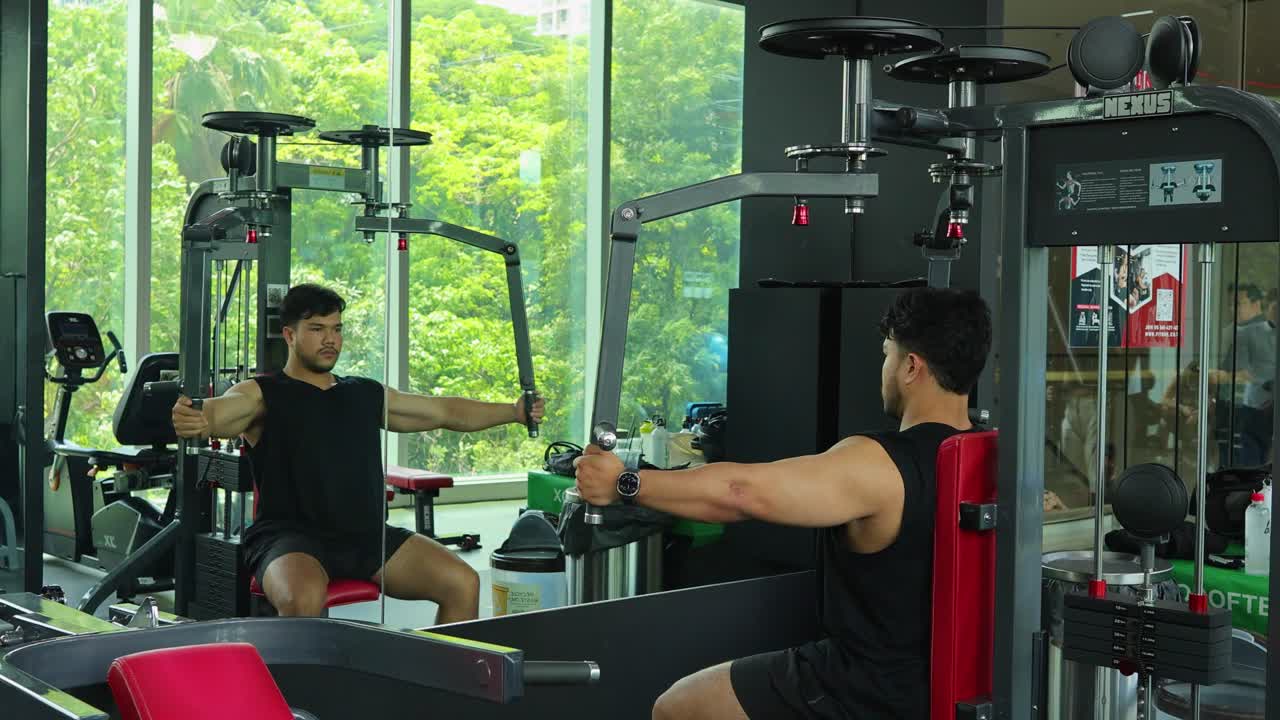 Young man in athletic wear performs chest fly exercise on machine in bright modern gym