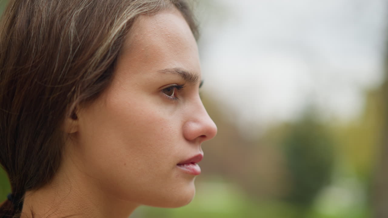 Close-up view of womans face turning and blinking eyes, subtle expression, natural beauty, soft focus, relaxed moment, outdoor setting, calm and serene expression, slow motion capture