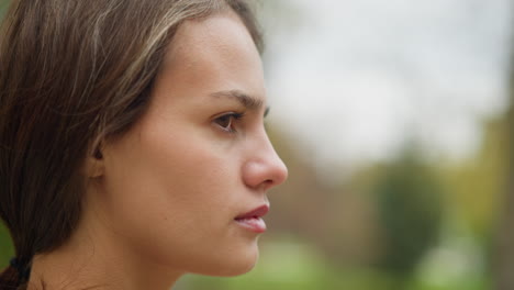 close-up view of womans face turning and blinking eyes, subtle expression, natural beauty, soft focus, relaxed moment, outdoor setting, calm and serene expression, slow motion capture