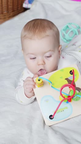 baby squeezes toy blocks while lying on belly and observing surroundings indoors