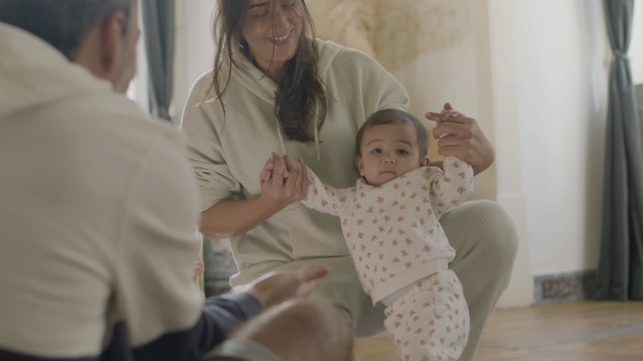 felices padres jóvenes enseñando a su linda niña a dar sus primeros pasos en casa 1