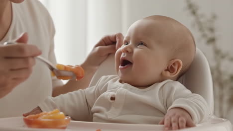 mother feeding her happy baby pureed food in a high chair