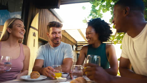 group of smiling multi-cultural friends eating breakfast outdoors at home making a toast together