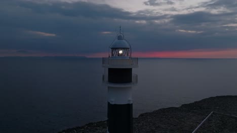 aerial close up view of cap d’artrutx lighthouse with fiery sunset sky, drone orbit
