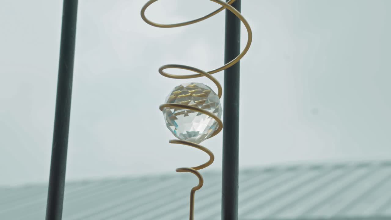 Crystal ball on a golden spiral wind spinner twisting and turning in front of a window. The faceted glass reflects light as it rotates