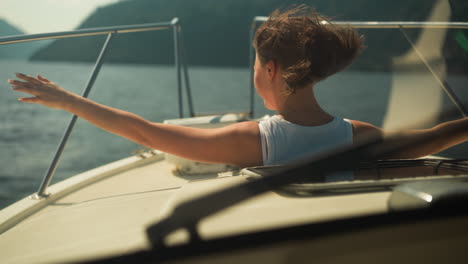 cheerful female stretches arms to sides looking out of hatch of yacht cabin. simulate flight and enjoy boat ride on vacation. water trip in summer