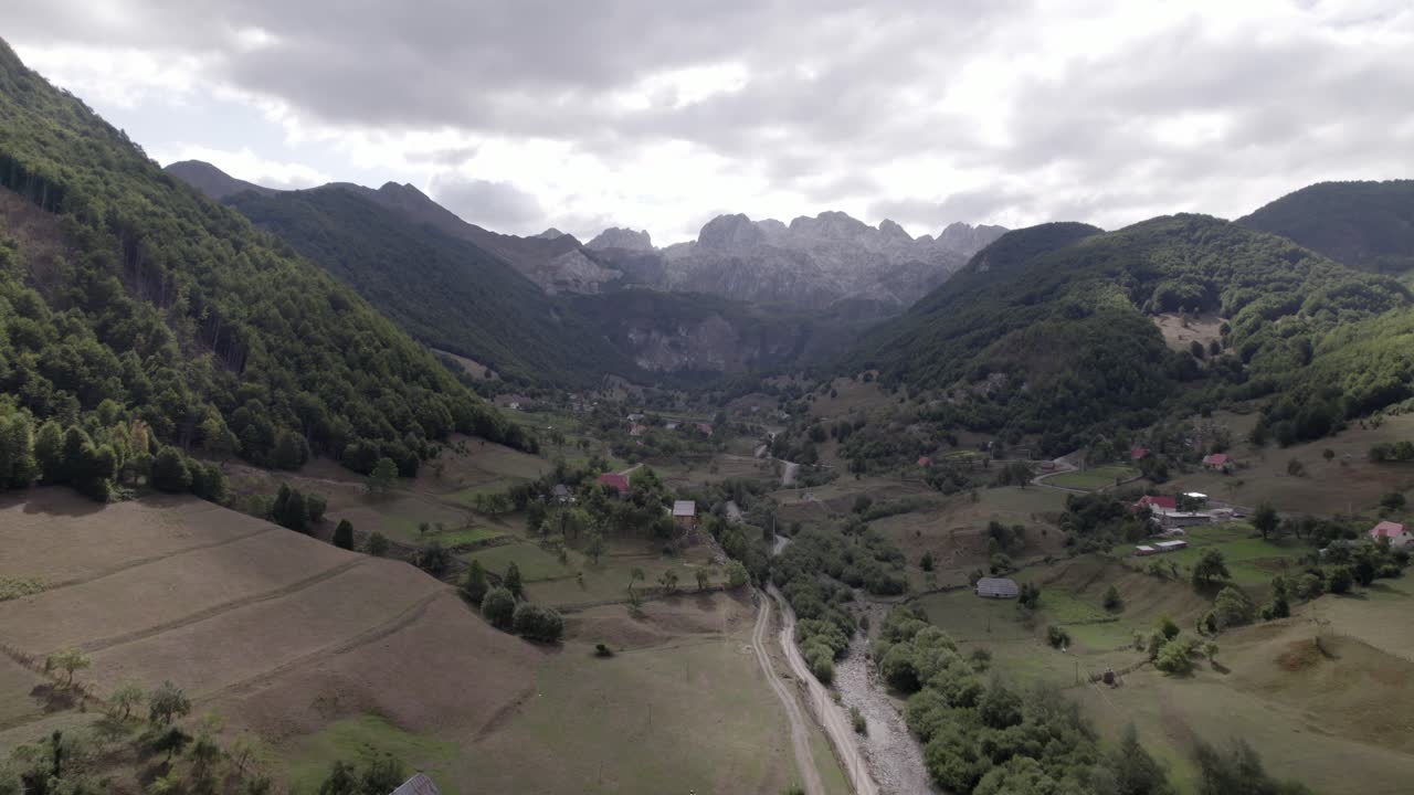 video drone del avion frontal avanzando sobre el valle de lepushë sobre el rio lëpusha, el sh20 en albania, se pueden ver casitas del pueblo, un cielo algo nublado y el rio seco