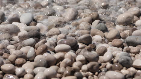 Foam-of-seawater-covering-pebbles-beach,-vacation-concept,-water-texture