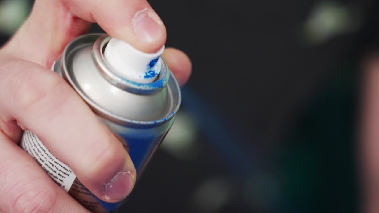 Hand pressing a spray paint can nozzle, releasing blue paint