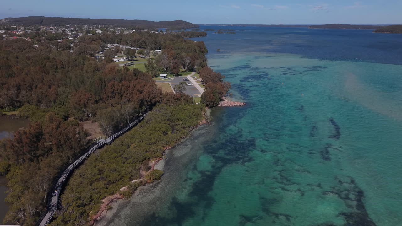 Boardwalk path through nature preserve, tropical waters ripple along shoreline with sandy textures and vibrant blues, Swansea Pirrita Island New South Wales