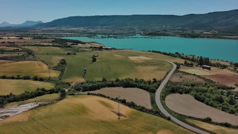 Abandoned-village-Esco-near-Zaragoza-with-contrasting-fields-and-a-turquoise-lake,-sunny-day,-aerial-view