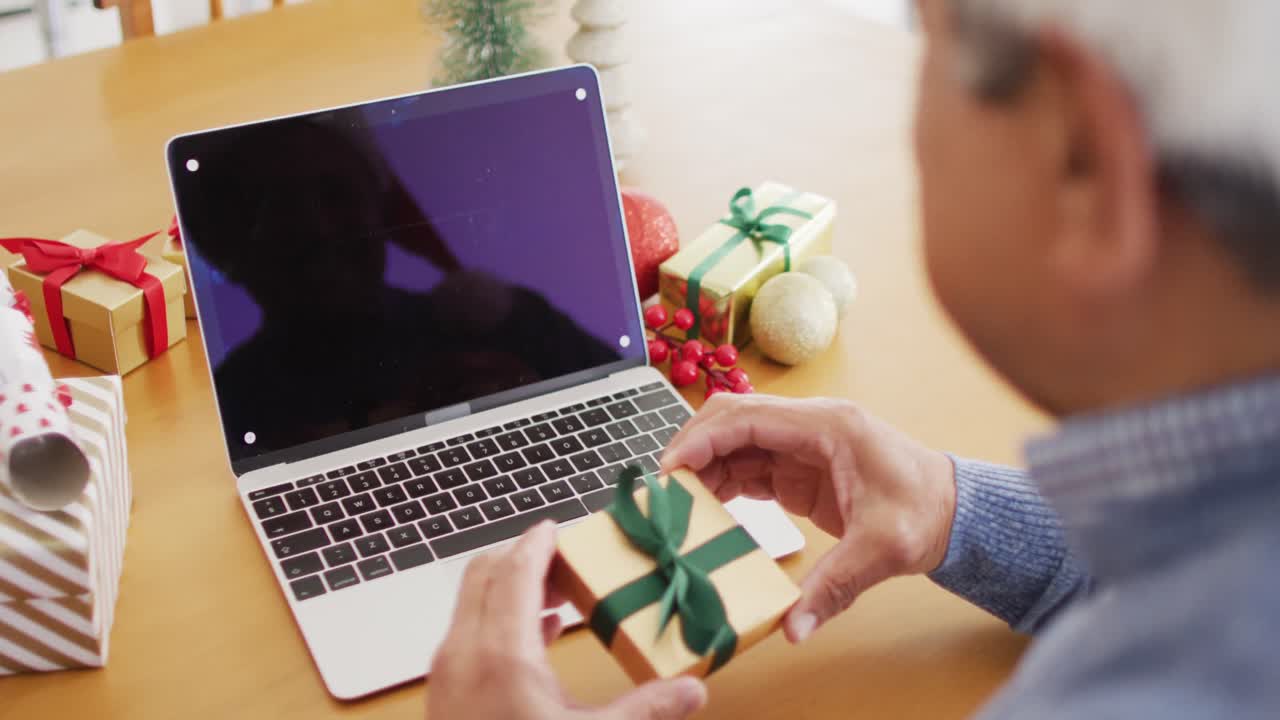 video de un hombre biracial mayor sosteniendo un regalo de navidad llamada de video portátil, copia espacio en la pantalla