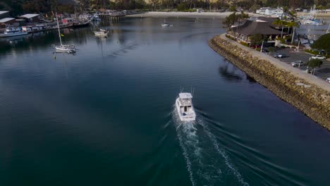 Rear-aerial-view-of-boat-entering-harbor-with-small-ripples-from-wake